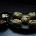 Steamed momos with dipping sauces on a dark plate