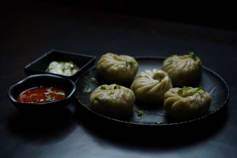 Steamed momos with dipping sauces on a dark plate